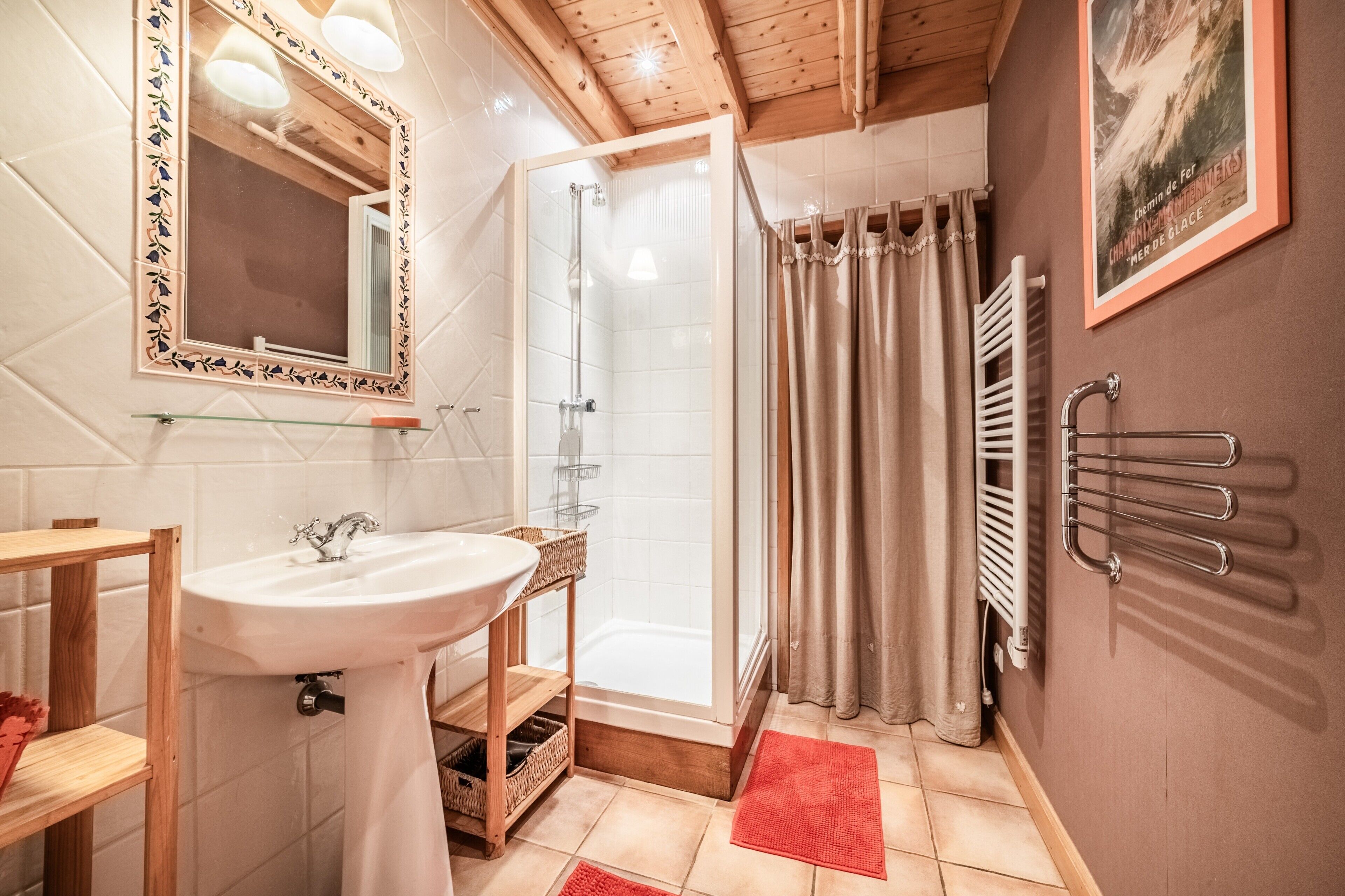 A bathroom with a white sink, mirror, shower, and a red bath mat.
