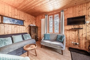 A wooden-paneled room with a sofa, armchair, television, and a window with curtains.
