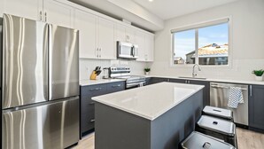 Une cuisine moderne dotée d’appareils électroménagers en acier inoxydable, d’un îlot central et offrant une vue sur les maisons grâce à une grande fenêtre.