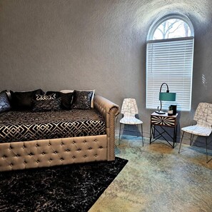 A room with a tufted sofa, two chairs, a small table with a lamp, and a window with blinds.