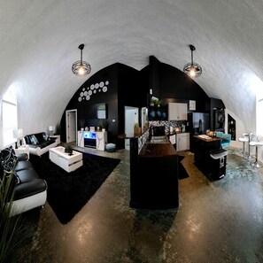 A spacious loft with a high ceiling, a kitchen area, a seating area with a sofa and coffee table, and a bar area with stools. - Dome Home at Lake Palestine: Unique Dome Rental in Bullard, Texas (Bullard)
