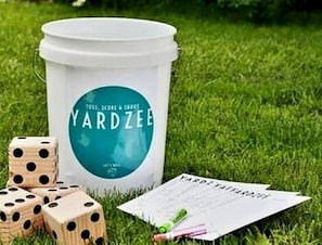 Un seau blanc portant l’inscription « YARDZEE », avec des dés et une carte, posé sur l’herbe.
