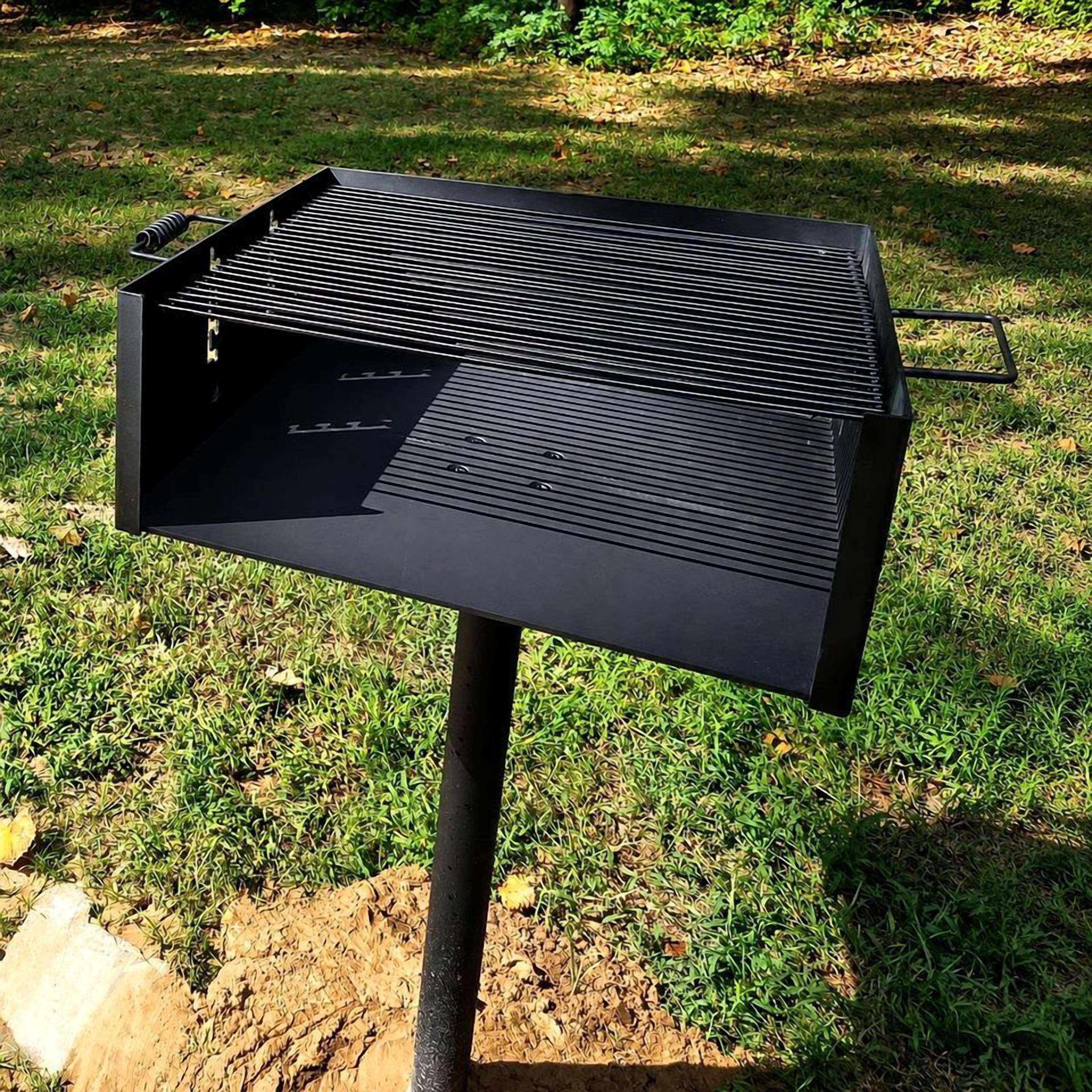 A black outdoor grill with a slanted lid, set on a grassy area with a dirt patch in the foreground.