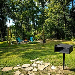 Un jardin avec un foyer, deux chaises bleues et un barbecue noir.