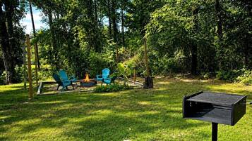 A backyard with a fire pit, two blue chairs, and a black grill.
