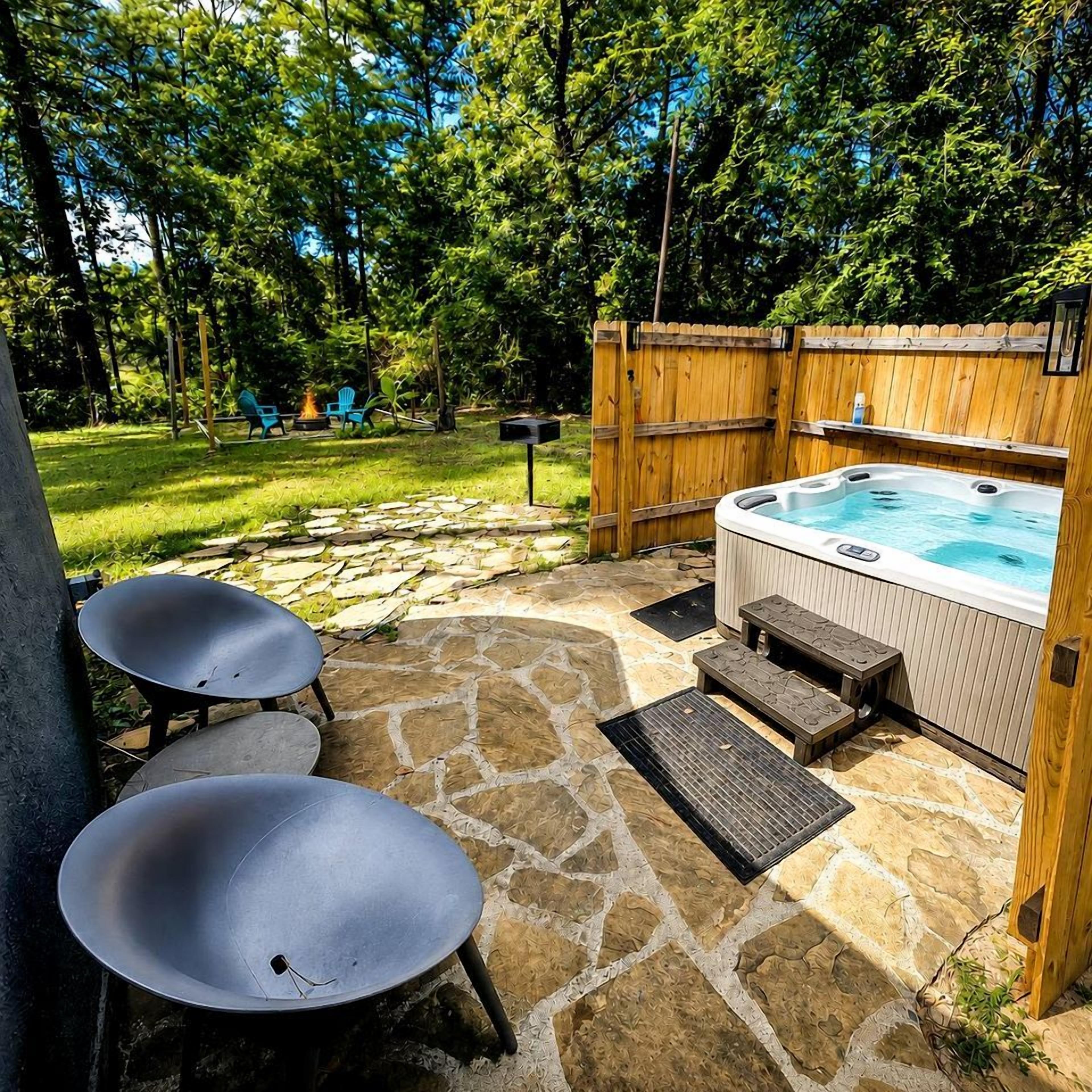 A hot tub with a stone patio, two metal chairs, and a wooden fence.