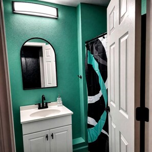 Une salle de bain avec un lavabo blanc, un miroir et un rideau de douche de couleur turquoise.