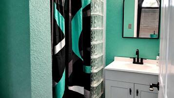 A bathroom with a shower curtain, a sink, a mirror, and a cabinet.