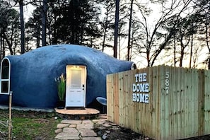 Kupolimainen rakennelma, jonka kyljessä on teksti ”THE DOME HOME”, ja jossa on ovi sekä pieni kuistialue.
