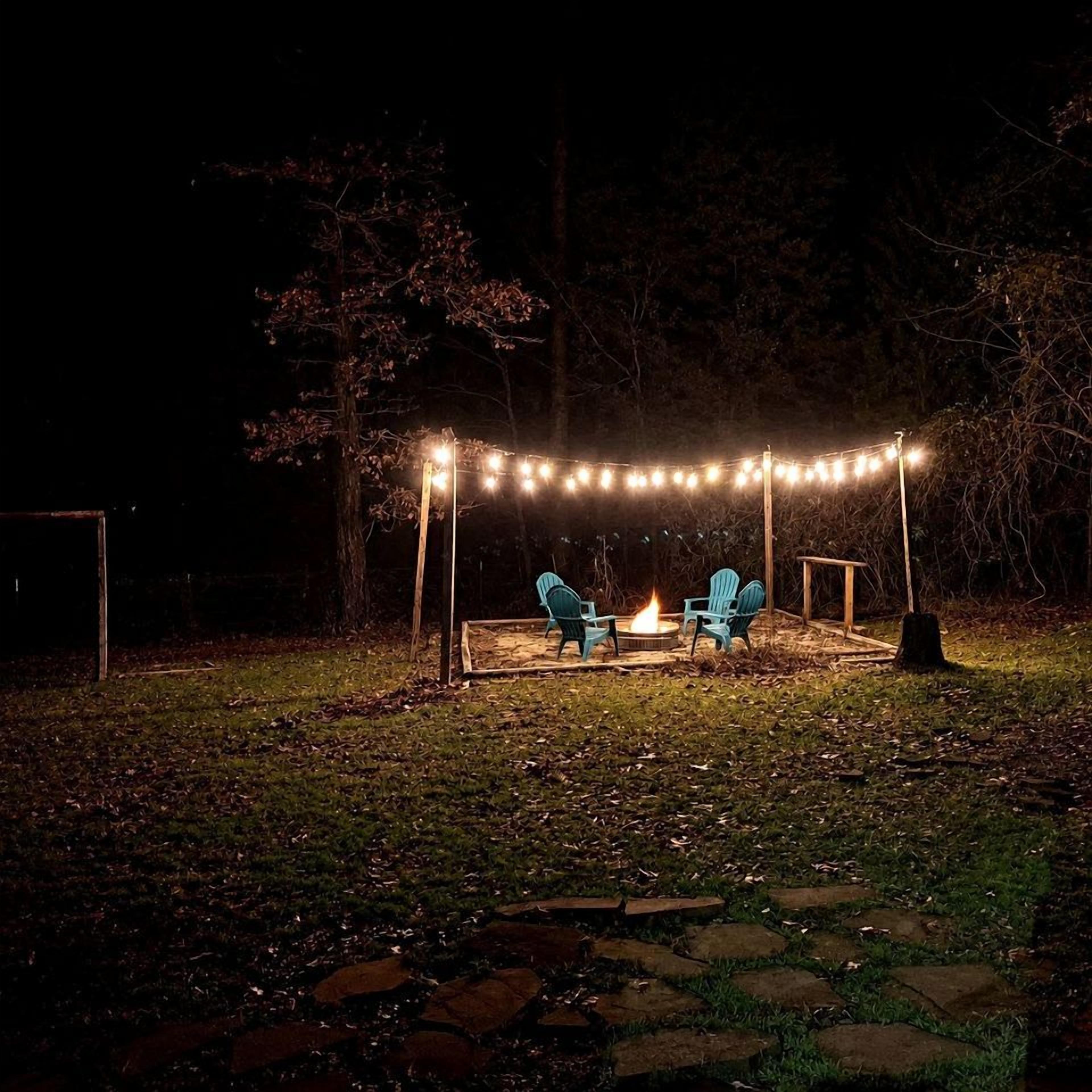 An outdoor seating area with chairs and a fire pit, surrounded by string lights.