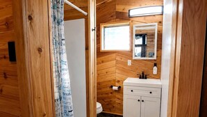 A compact bathroom with wooden walls, a white sink, and a mirror above it. - Fish Cabin at the Pines: Cozy Cabin near Lake O' the Pines in Jefferson, Texas (Jefferson)