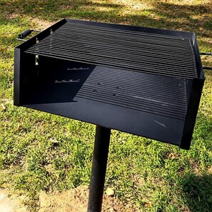 Una barbacoa negra amb una superfície plana i reixes de ventilació als laterals, damunt un terreny enjardinat.