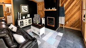 A modern living room with a leather sofa, a fireplace, and a herringbone-patterned wall. - Fish Cabin at the Pines: Cozy Cabin near Lake O' the Pines in Jefferson, Texas (Jefferson)
