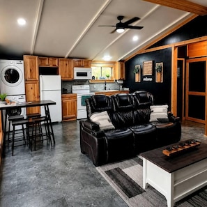 A modern kitchen with wooden cabinets, a dining area with a leather sofa, and a ceiling fan. - Fish Cabin at the Pines: Cozy Cabin near Lake O' the Pines in Jefferson, Texas (Jefferson)