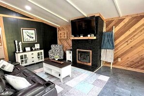 Ein Wohnzimmer mit Kamin, einer Couch, einem Fernseher und einem gemusterten Sessel.