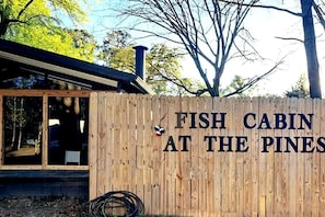 A wooden cabin with a sign that reads 'FISH CABIN AT THE PINES.'