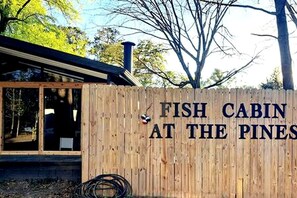 Une cabane en bois avec une pancarte sur laquelle on peut lire : « CABANE DE PÊCHE, AUX PINS ».