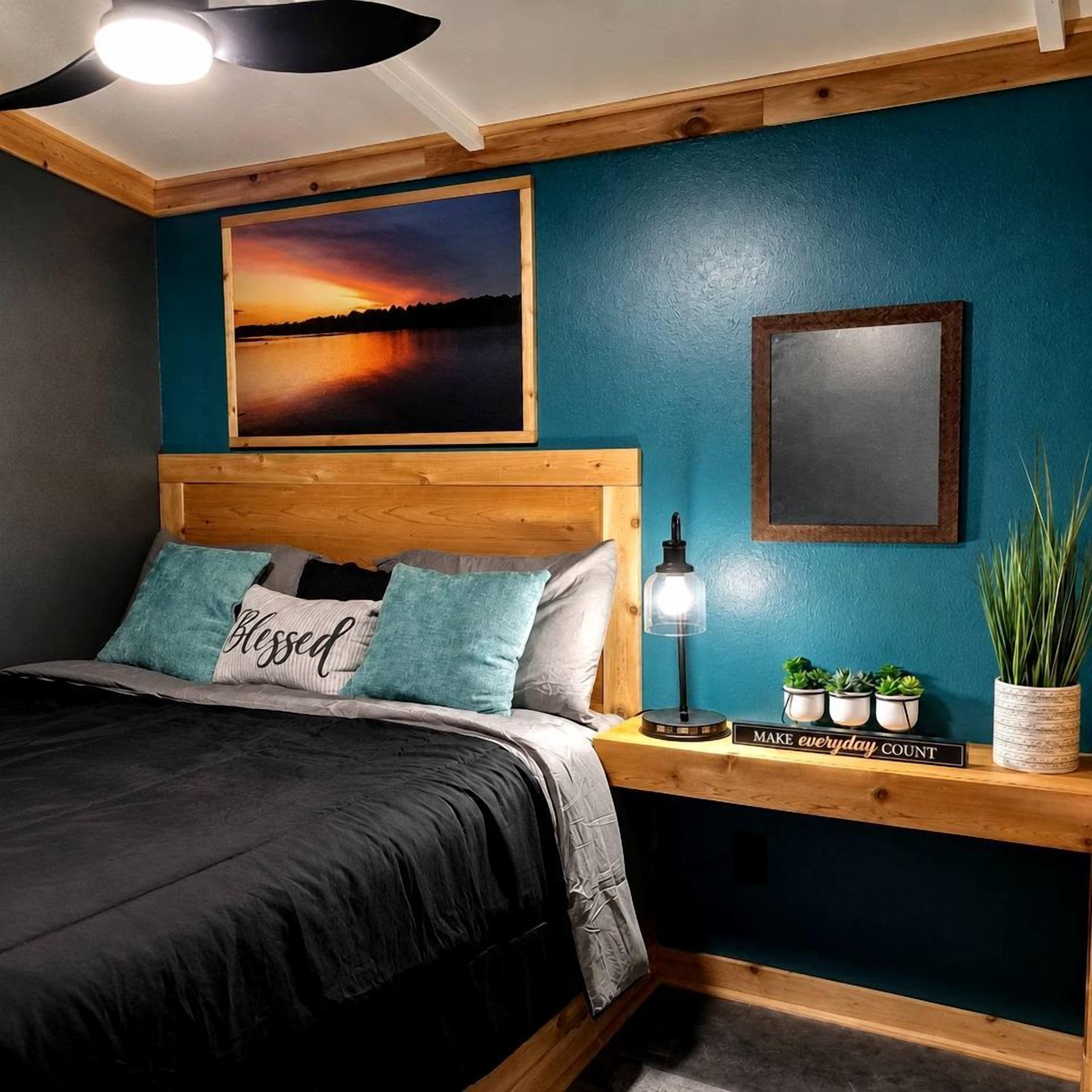 A bedroom with a bed, a nightstand with a lamp, a framed picture, and a potted plant.