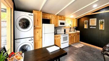 A compact kitchen with wooden cabinets, a washing machine, a refrigerator, a microwave, and a stove.