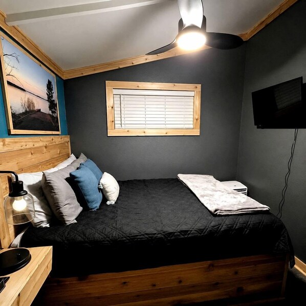 A bedroom with a bed, a window, a painting, and a ceiling light fixture.
