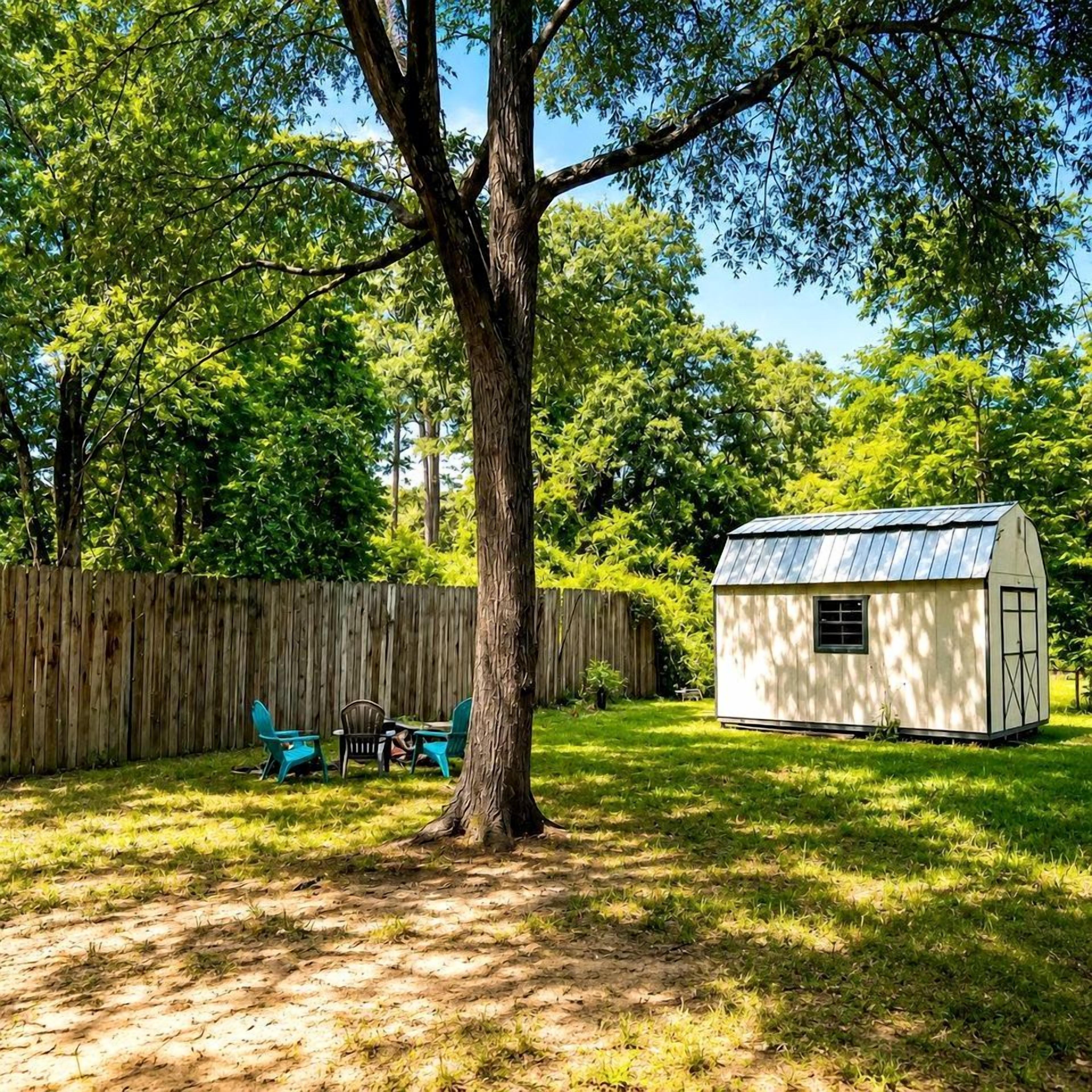 A fenced yard with a tree, a small shed, and a table with chairs.