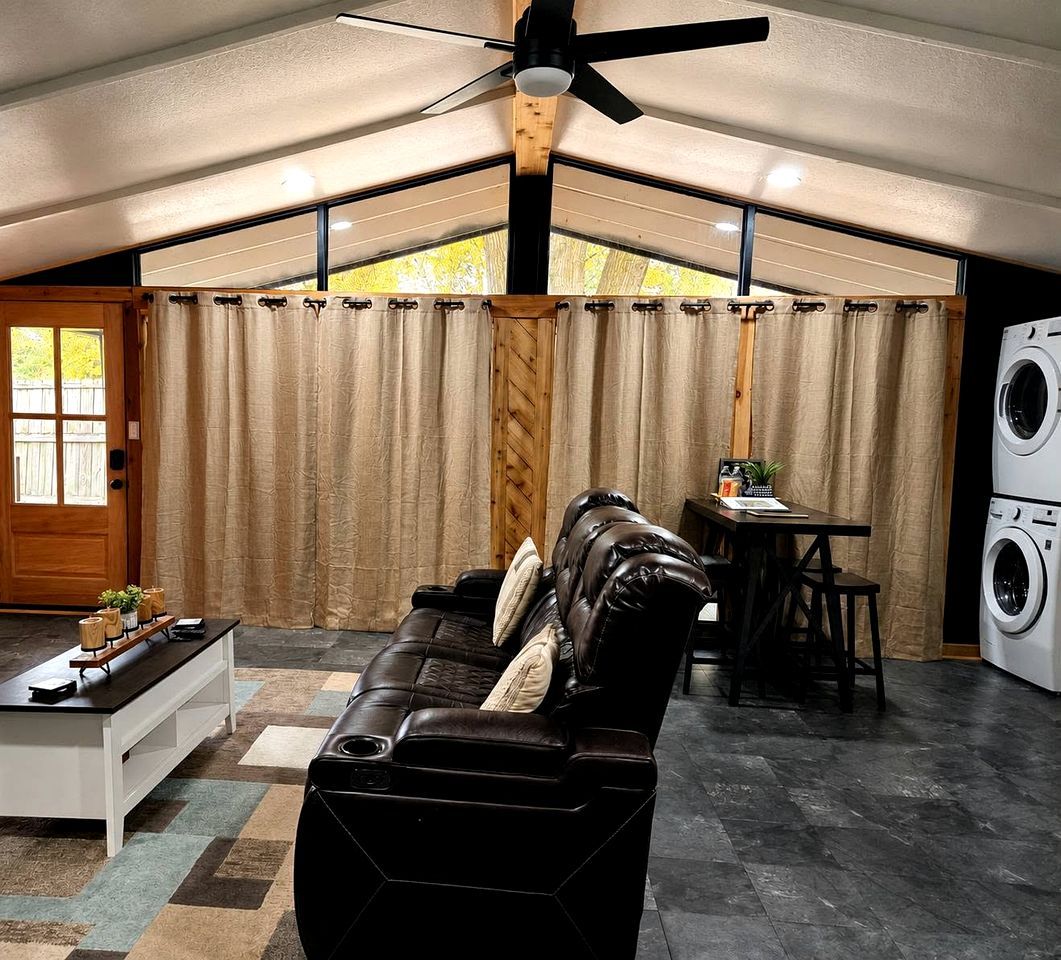 A modern living room with a leather sofa, a dining table, a ceiling fan, and a washing machine.