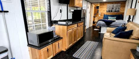 Cocina compacta con encimera negra, armarios de madera y microondas integrado.