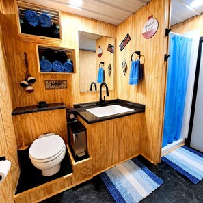 A wooden-themed bathroom with a sink, toilet, and a mirror. - Keepin It Reel on Caddo Lake: Incredible Houseboat in Uncertain, Texas (Uncertain)