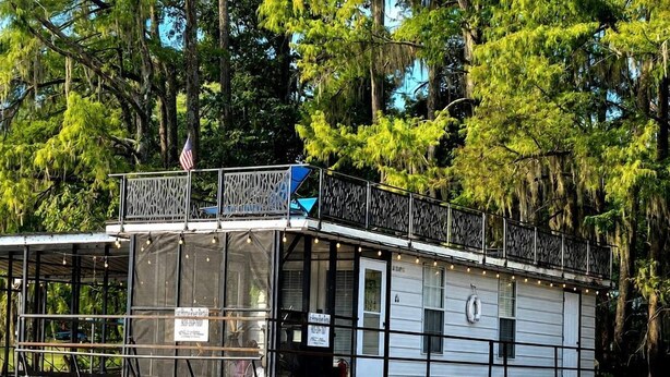 A houseboat with a covered deck, windows, and a flag.
