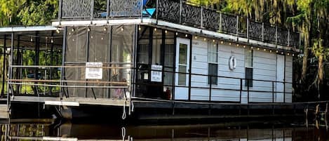 A houseboat with a covered deck, windows, and a flag.