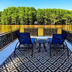 Une terrasse avec deux chaises et une petite table, donnant sur une étendue d’eau, avec des arbres en arrière-plan.