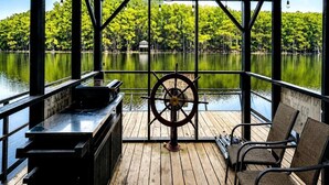 A covered deck with a wooden floor, a steering wheel, and two chairs.