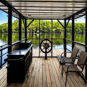 A covered deck with a wooden floor, a steering wheel, and two chairs. - Keepin It Reel on Caddo Lake: Incredible Houseboat in Uncertain, Texas (Uncertain)