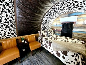 Une chambre avec un lit à motifs de vaches, un canapé en cuir et une petite table sur laquelle est posée une plante.