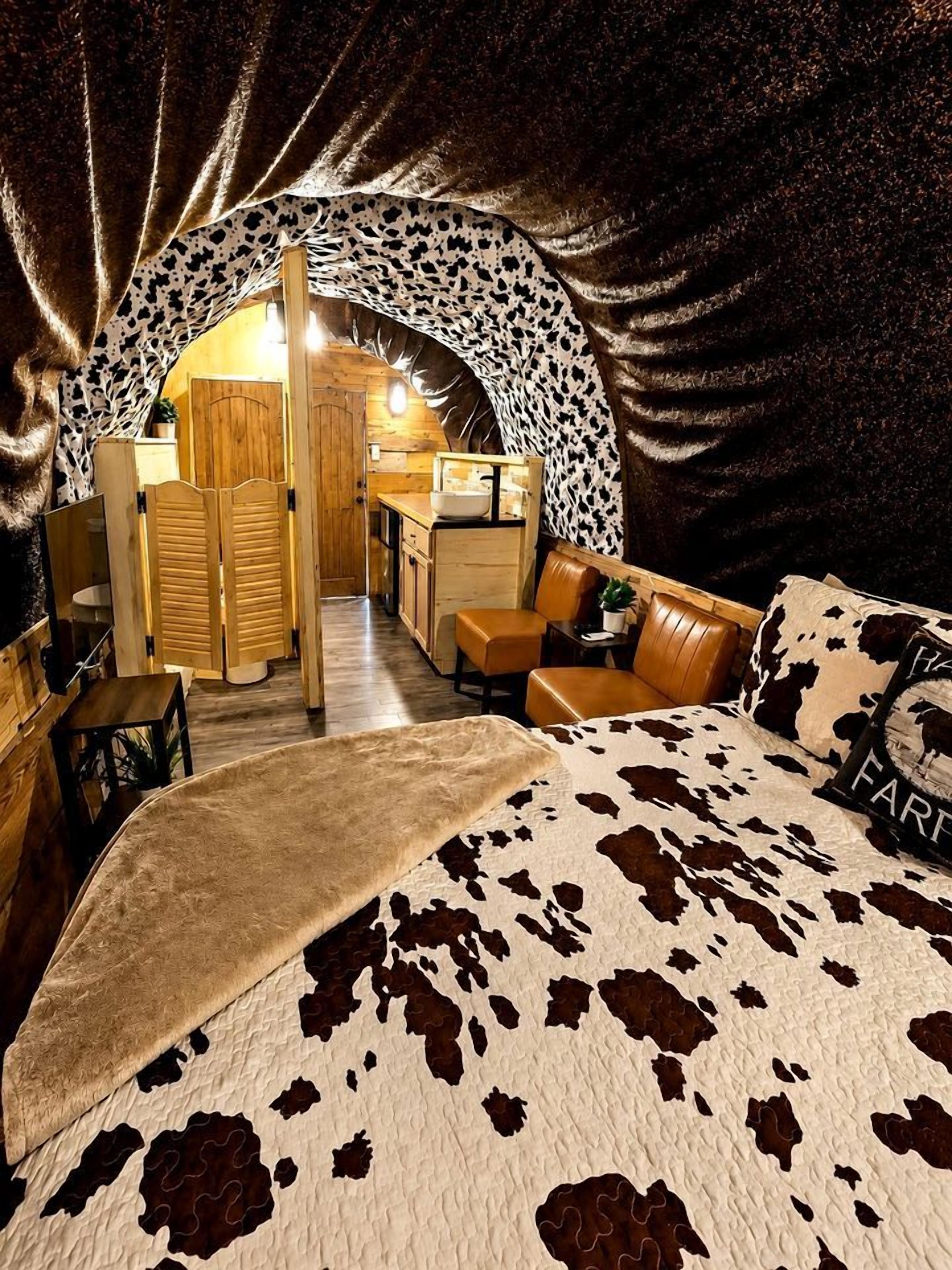 Un dormitorio acogedor con colcha de estampado de vaca, una puerta de madera que da a una kitchenette y un sofá de cuero.