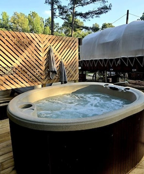 Un jacuzzi en un entorno exterior con una terraza de madera y una zona cubierta al fondo.