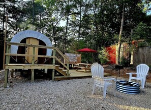 Une structure rustique en bois, dotée d’une entrée couverte, d’une terrasse en bois et de deux chaises Adirondack blanches.
