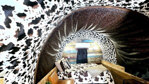 A cozy, cow-print themed interior with a bed, seating area, and a wooden floor.