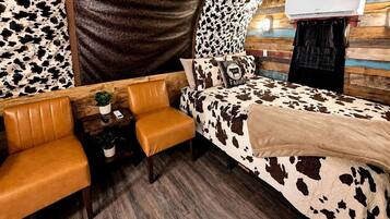 A room with a cow print bedspread, a sofa, a small table with a plant, and an air conditioning unit mounted on the wall.