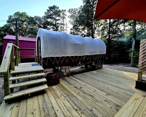 A covered wooden deck with a covered wagon, steps leading up to it, and a red canopy overhead.