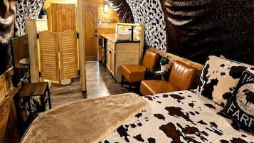 Un dormitorio acogedor con colcha de estampado de vaca, una puerta de madera que da a una kitchenette y un sofá de cuero.