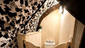 Un escalier en bois mène à une petite salle de bain fermée, équipée de toilettes et d’une étagère.