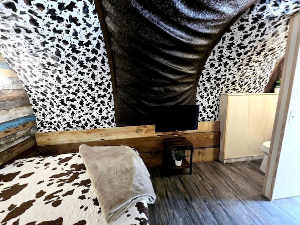 Una habitación acogedora con un tapete estampado de piel de vaca, un banco de madera, una mesita con una planta y un televisor fijado a la pared.