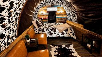 A cozy interior with a cowhide wall, a bed with a cowhide blanket, a leather sofa, and a cowhide rug.