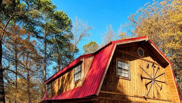 Un edificio de estilo rústico tipo granero, con techo rojo, revestimiento de madera y un garaje con puertas rojas.