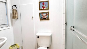 A bathroom with a toilet, a sink, and a shower. There are three framed pictures on the wall. - Rustic Retreat near Lake O the Pines: Gorgeous Barn in Warlock, Texas (Warlock)