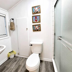 A bathroom with a toilet, a sink, and a shower. There are three framed pictures on the wall. - Rustic Retreat near Lake O the Pines: Gorgeous Barn in Warlock, Texas (Warlock)