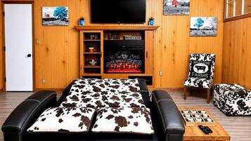 Ein gemütliches Zimmer mit einem großen Bett, einem Kamin, einem Fernseher und einem Sessel mit Kuhmuster.