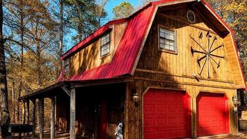 A rustic barn-style building with a red roof, wooden siding, and a garage with red doors.