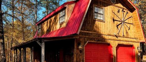 A rustic barn-style building with a red roof, wooden siding, and a garage with red doors.